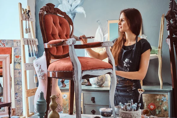 Artista feminina pintando cadeira vintage na cor branca com pincel na oficina . — Fotografia de Stock