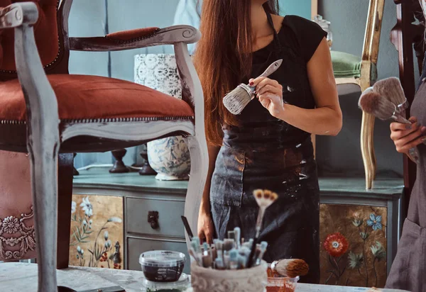 Artiste féminine avec son assistante dans les tabliers peinture chaise vintage avec pinceau dans l'atelier . — Photo