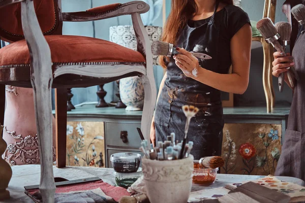 Künstlerin mit ihrem Assistenten in Schürzen bemalt Vintage Stuhl mit Pinsel in der Werkstatt. — Stockfoto
