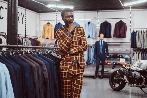 Elegantemente vestido homem africano posando com a mão no queixo, enquanto em pé em uma loja de moda masculina clássico . — Fotografia de Stock
