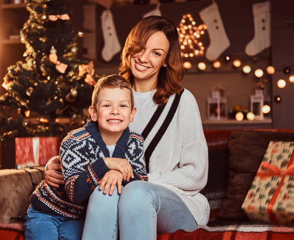 妈妈拥抱她可爱的小男孩, 而坐在沙发上装饰的房间在圣诞节时间. — 图库照片