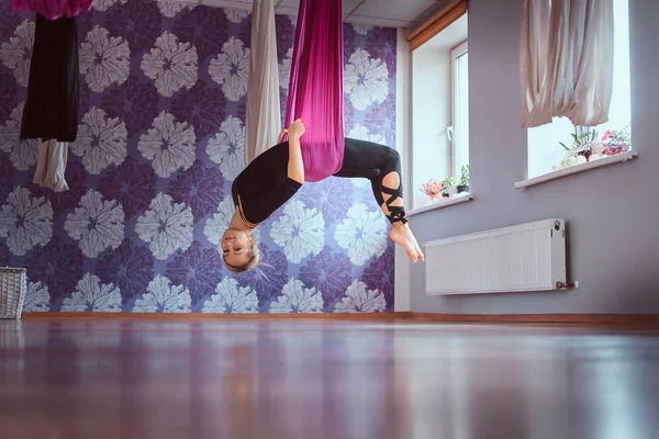 Mujer joven practicando yoga aéreo en hamaca púrpura en club de fitness . —  Fotos de Stock