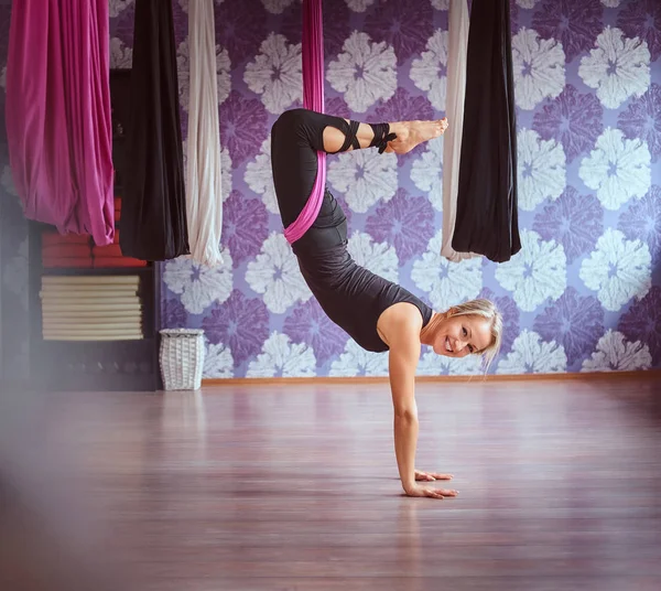 Junge Frau praktiziert Aerial Yoga in lila Hängematte im Fitnessclub. — Stockfoto