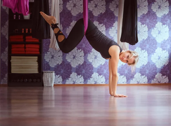Mujer joven practicando yoga aéreo en hamaca púrpura en club de fitness . — Foto de Stock