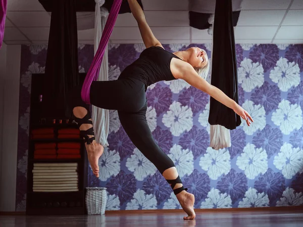 Junge Frau praktiziert Aerial Yoga in lila Hängematte im Fitnessclub. — Stockfoto