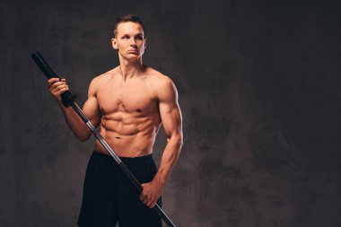 Bir halter tutarak ve uzak koyu arka plan üzerinde seyir yakışıklı bir genç vücut portresi.