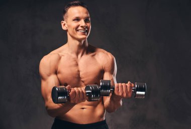 Koyu arka plan üzerinde dumbbells ile egzersiz yaparak kas vücut ile genç gömleksiz vücut geliştirmeci.