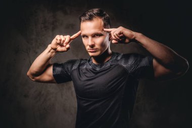 Dalgın genç sporcu portresi onun tapınak ve kameraya bakarak işaret parmakları koymak.