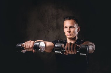 Karanlık bir arka plan üzerinde dumbbells ile egzersiz yaparak spor giyim giyen genç bir vücut geliştirmeci.