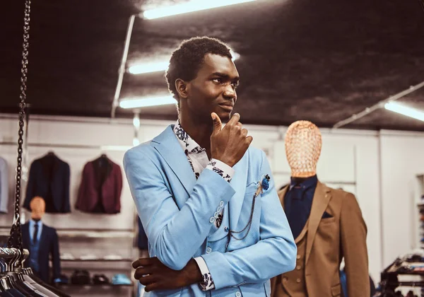 Elegant gekleideter afrikanischer Mann posiert mit der Hand am Kinn, während er in einem klassischen Herrengeschäft steht. — Stockfoto