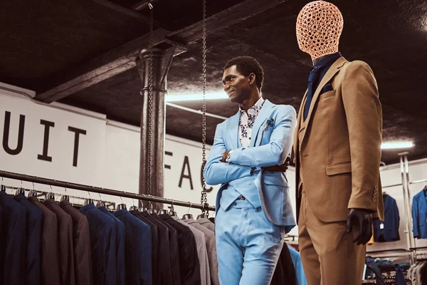 Elegantemente vestido homem afro-americano posando com braços cruzados perto de manequim em uma loja de moda masculina clássica . — Fotografia de Stock