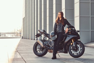 Güneşli bir günde bir bina dışında onun superbike yaslanmış bir güzel motorcu kız.
