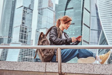 Moskova şehir içinde gökdelenler önünde bir smartphone kullanarak yüzünde dövmeler ile şık giyimli kızıl öğrenci kız.