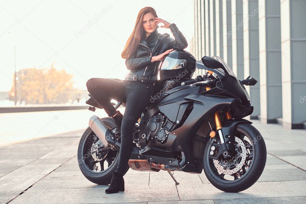 A beautiful biker girl leaning on her superbike outside a building.