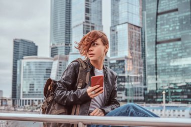 Moskova şehir içinde gökdelenler önünde bir smartphone kullanarak yüzünde dövmeler ile şık giyimli kızıl öğrenci kız.