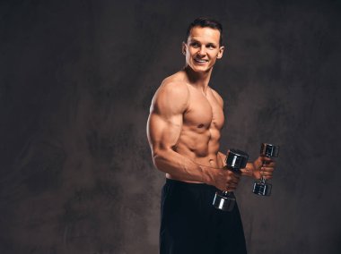 Koyu arka plan üzerinde dumbbells ile egzersiz yaparak kas vücut ile genç gömleksiz vücut geliştirmeci.