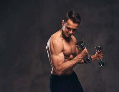 Koyu arka plan üzerinde dumbbells ile egzersiz yaparak kas vücut ile genç gömleksiz vücut geliştirmeci.
