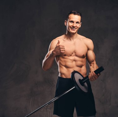 Bir halter tutarak ve uzak koyu arka plan üzerinde seyir yakışıklı bir genç vücut portresi.