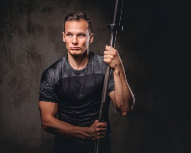 Bir halter tutarak ve uzak koyu arka plan üzerinde seyir yakışıklı bir genç vücut portresi.