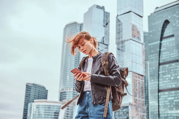 Moskova şehir içinde gökdelenler önünde bir smartphone kullanarak yüzünde dövmeler ile şık giyimli kızıl öğrenci kız.