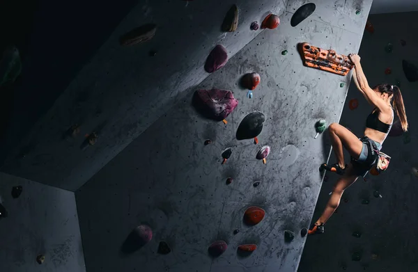 Mladá žena v kraťasy a sportovní podprsenku na bouldering stěna uvnitř. — Stock fotografie