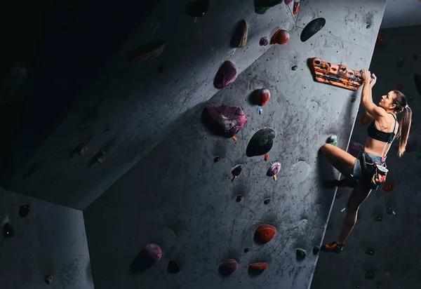 Junge Frau in kurzen Hosen und Sport-BH beim Training an einer Boulderwand drinnen. — Stockfoto