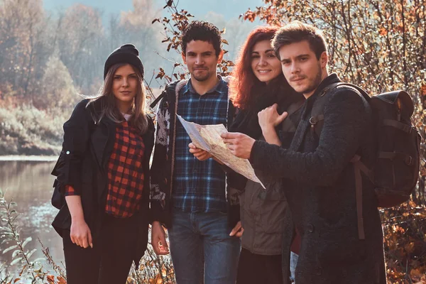 Group of young friends hiking in autumn colorful forest, looking at map and planning hike.