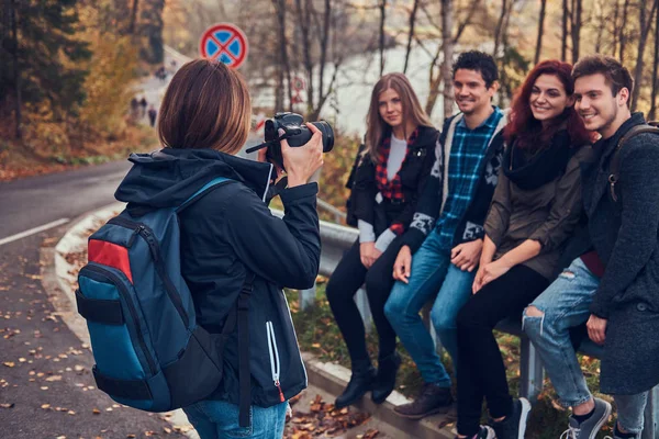 Meisje dat neemt een foto van haar vrienden. Groep jonge vrienden zittend op de leuning in de buurt road. — Stockfoto