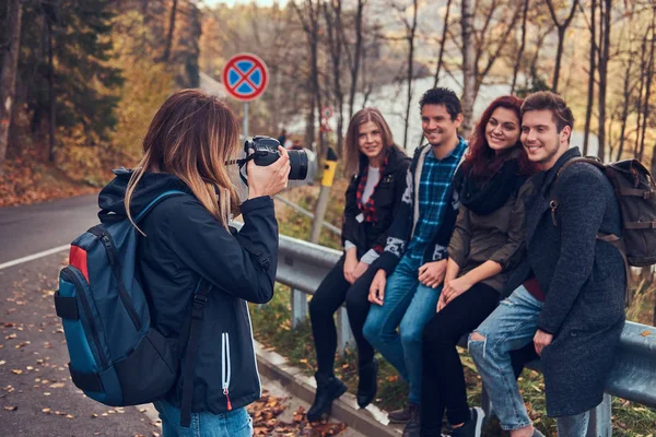 Meisje dat neemt een foto van haar vrienden. Groep jonge vrienden zittend op de leuning in de buurt road. — Stockfoto