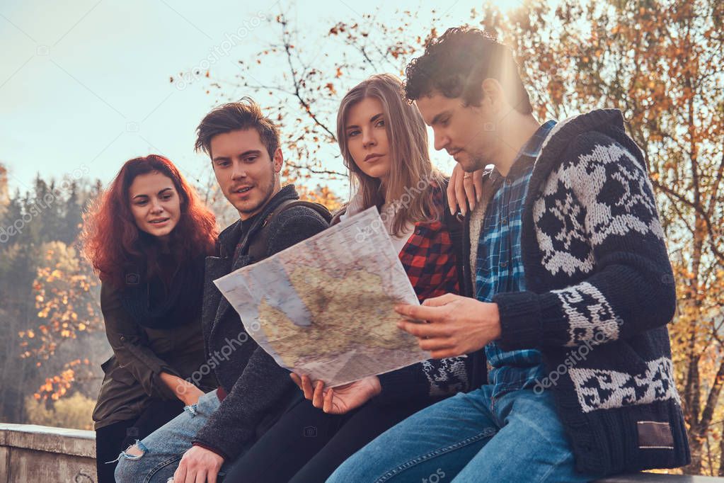 Photo of young friends looking at map and planning trip at autumn forest.