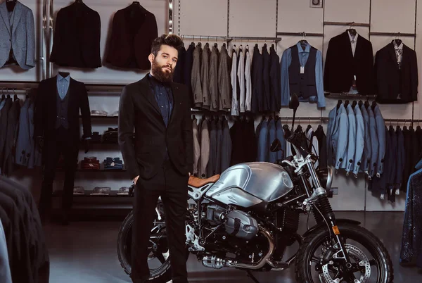 胡子时尚男子身着黑色西装摆在口袋附近复古运动摩托车在男装店. — 图库照片