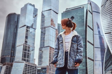 Yüzünde trendy dövmeli bir hippi kız bulutlu sabah Moskova şehir içinde gökdelenler önünde müzik dinlerken kulaklık giyen giyinmiş.