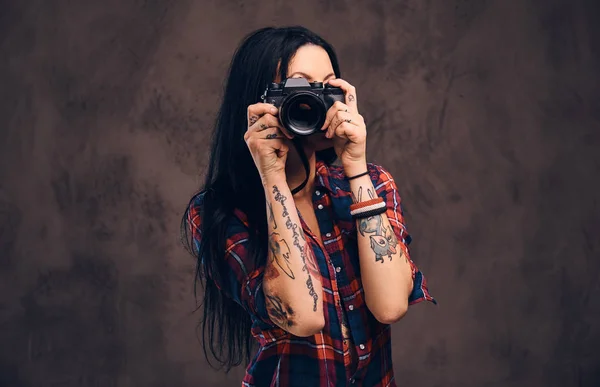 Tattooed girl taking a photo looking at camera in a studio.
