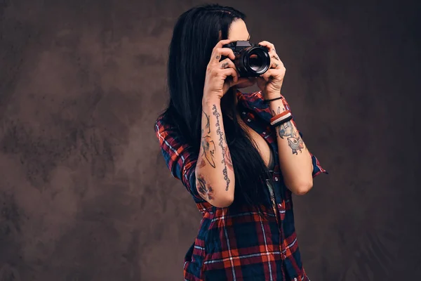 Tattooed girl taking a photo looking at camera in a studio.