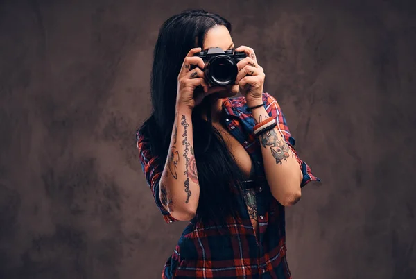 Tattooed girl taking a photo looking at camera in a studio.