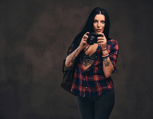 Seducente ragazza hipster tatuata con una camicia rossa a quadri sbottonata in posa con una fotocamera . — Foto Stock
