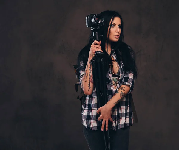 Sedutor tatuado menina vestindo um desabotoado verificado camisa menina posando com um câmara . — Fotografia de Stock