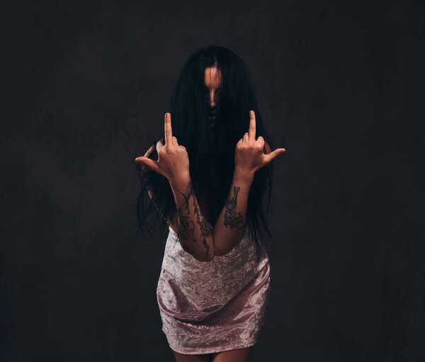 Bad tattooed girl wearing a nightie shows middle finger, fuck you with a sign.
