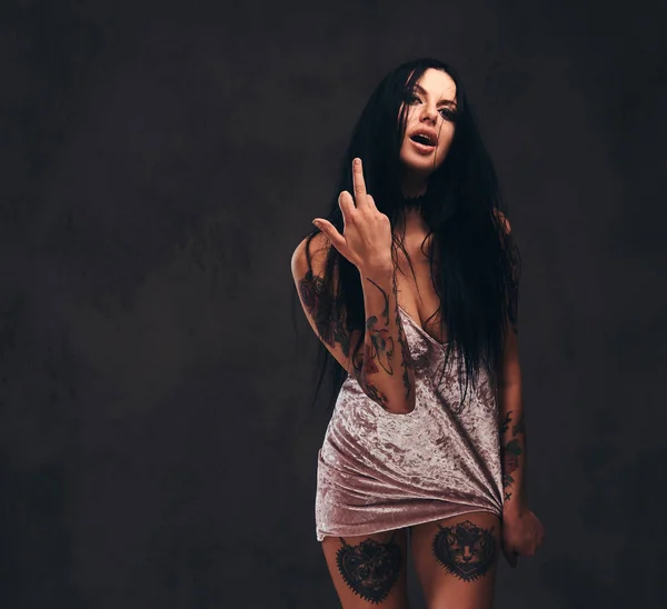 Brutta ragazza tatuata che indossa una camicia da notte mostra il dito medio, scoparti con un segno . — Foto Stock