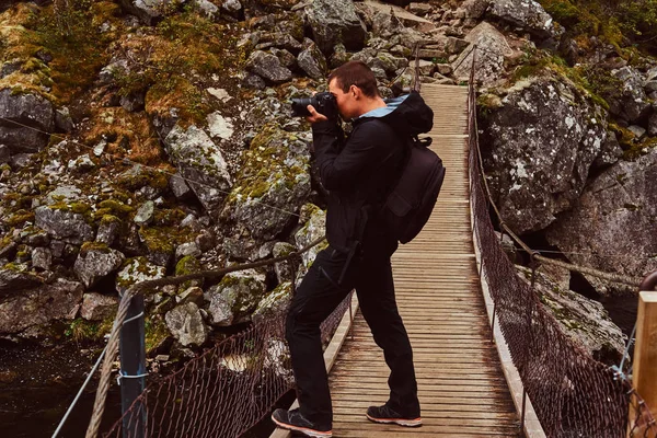 Φύση φωτογράφος τουριστικά με τη φωτογραφική μηχανή πυροβολεί ενώ στέκεται σε μια ξύλινη γέφυρα. Νορβηγία. — Φωτογραφία Αρχείου