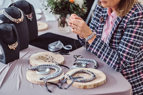 Элегантно одетая женщина делает ожерелья ручной работы, работая с иглами и нитками в мастерской . — стоковое фото