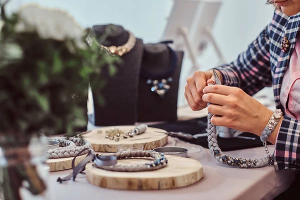 Femme élégamment habillée fabrique des colliers faits à la main, travaillant avec des aiguilles et du fil dans l'atelier . — Photo