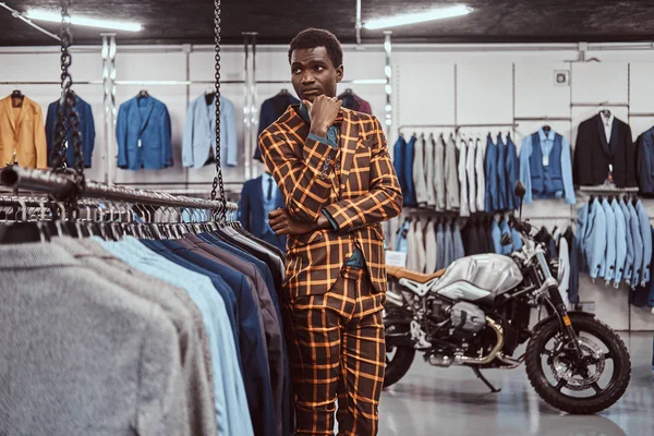 Элегантно одетый африканский мужчина позирует с рукой на подбородке, стоя в классическом магазине мужской одежды . — стоковое фото