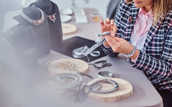 Elegantly dressed woman makes handmade necklaces, working with needles and thread in workshop. — Stock Photo, Image