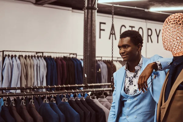 Элегантно одетый афроамериканец, опирающийся на манекен в классическом магазине мужской одежды . — стоковое фото