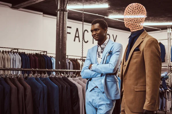 Элегантно одетый афроамериканец позирует со скрещенными руками возле манекена в классическом магазине мужской одежды . — стоковое фото