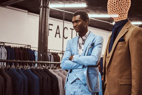 Elegant klädda afroamerikansk man poserar med korsade armar nära skyltdocka i en klassiska herrkläder butik. — Stockfoto