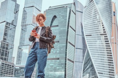 Moskova şehir içinde gökdelenler önünde bir smartphone kullanarak yüzünde dövmeler ile şık giyimli kızıl öğrenci kız.