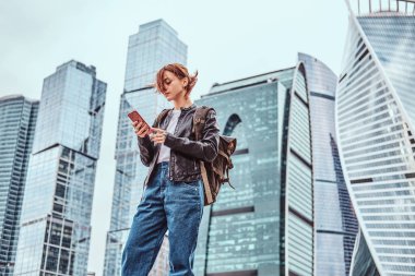 Moskova şehir içinde gökdelenler önünde bir smartphone kullanarak yüzünde dövmeler ile şık giyimli kızıl öğrenci kız.