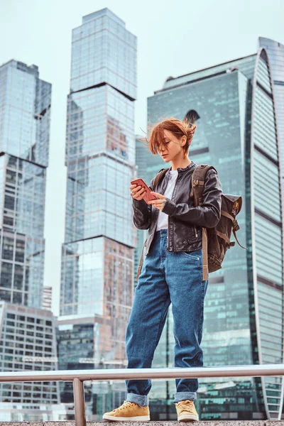 Moskova şehir içinde gökdelenler önünde bir smartphone kullanarak yüzünde dövmeler ile şık giyimli kızıl öğrenci kız.